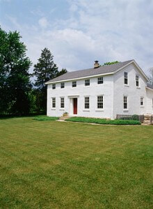 EXTERIORS: Two-story single family stucco Georgian Colonial farmhouse, built in 1841, restored, lawn, plain and simple, vertical version with more picket fence to right, ground cover near house